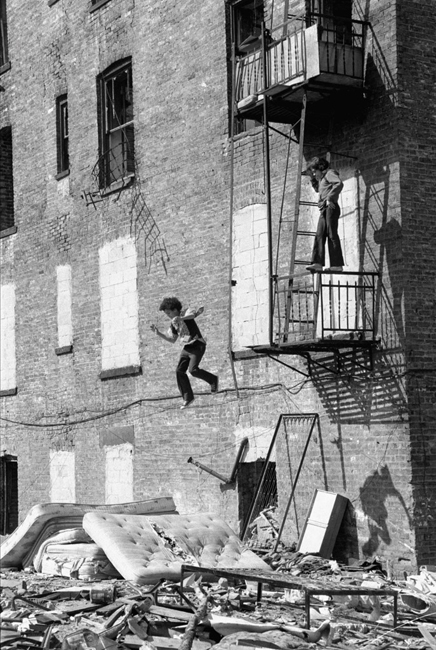 A street play photograph by Martha Cooper of a boy jumping from fire escape at the Lower East Side.