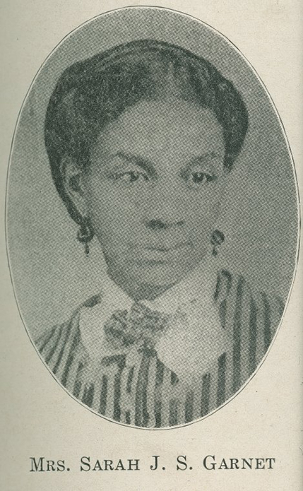 A black and white formal portrait photograph of a Black woman wearing a striped dress or waistcoat, lace and ribbon collar, and earrings.