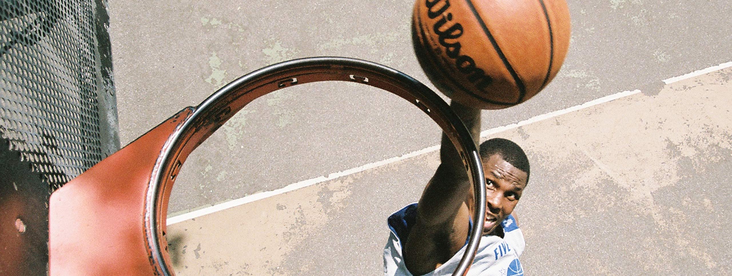 View from above a basketball hoop without a net, where a player is seen about to dunk a basketball through the hoop