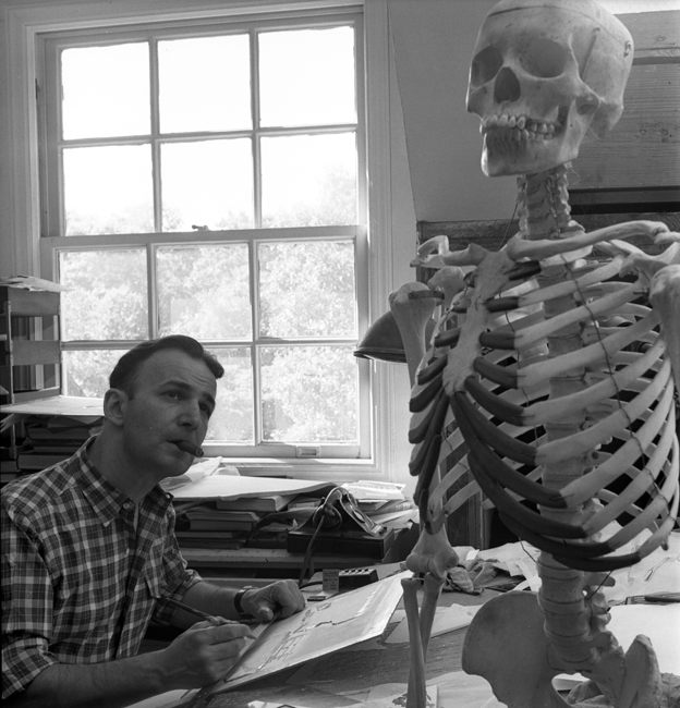 Dr. Frank Netter sits at a desk, smoking a cigar and drawing a human skeleton model that sits in front of him.