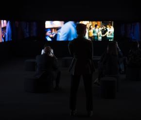  The silhouetted image of a woman standing in front of several screens showing blurred images of films.