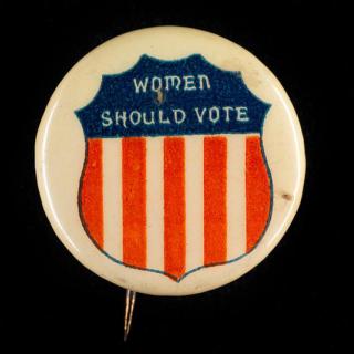 Women’s Suffrage button that says “Women Should Vote” with an image of shield with the red, white, and blue coloring of the American flag. 