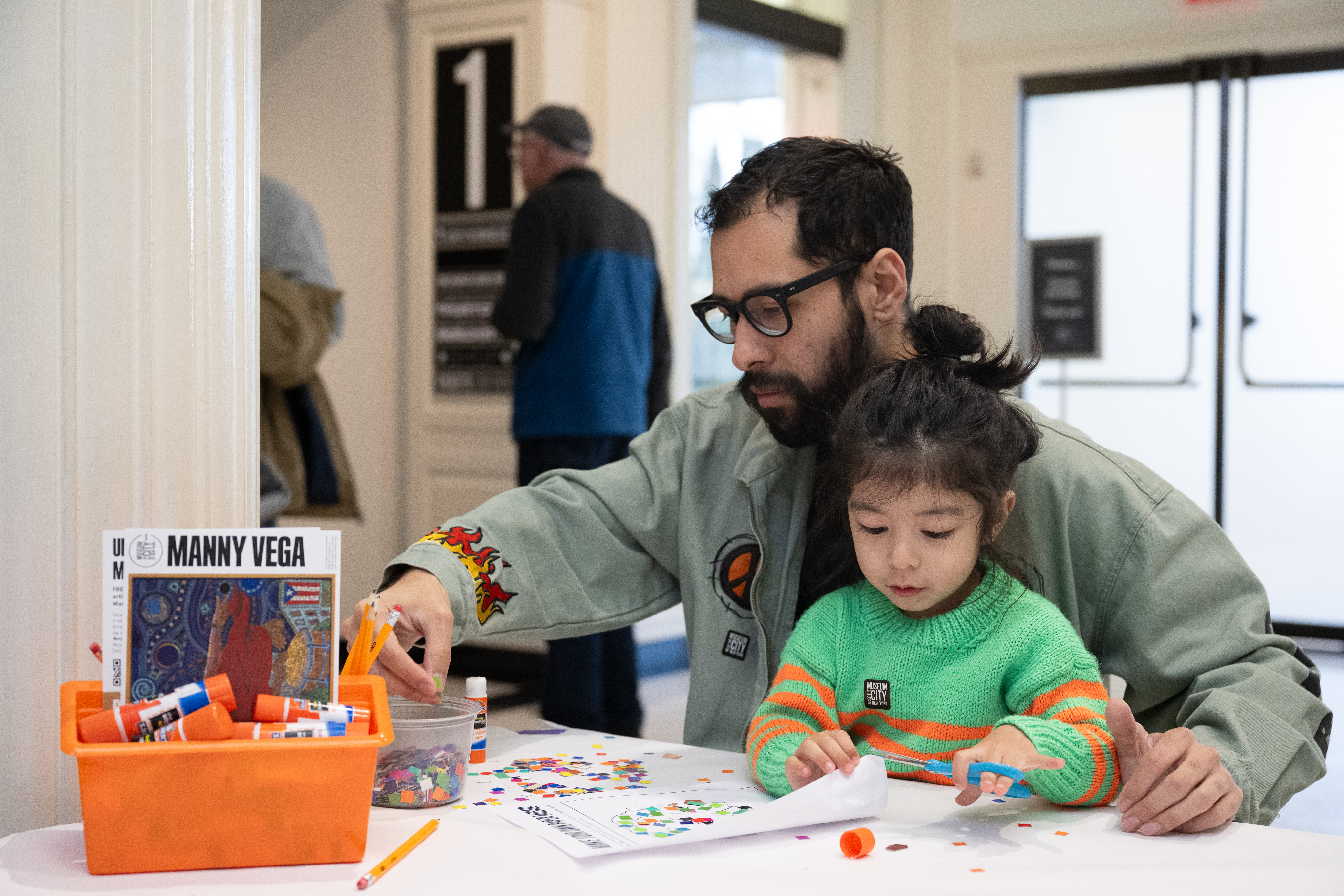 A man in glasses and a small child make art at a table. 
