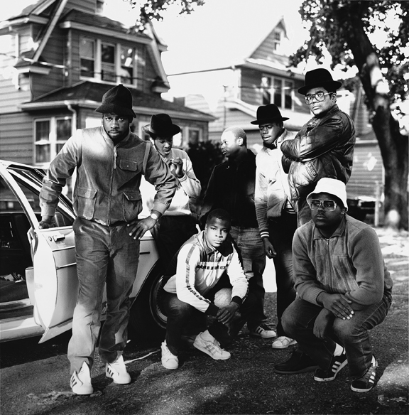 Black and white photograph featuring Run DMC posing in front of a car on a residential street.
