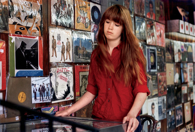 Color photograph of a girl in a red shirt sifting through records in a music store.