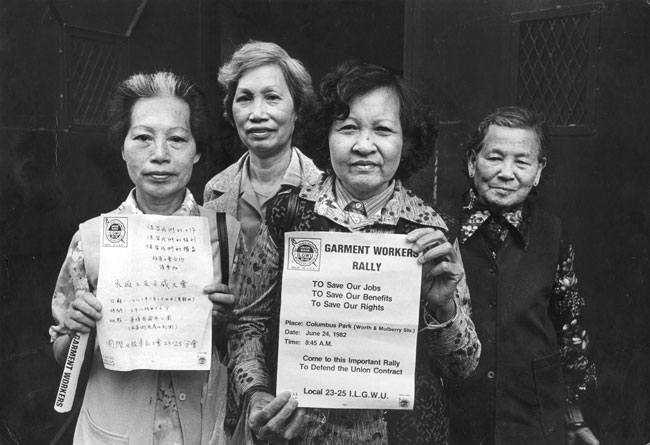 Four members of the ILGWU Local 23-25 who are on strike hold up flyers in Chinese and English for the June 24, 1982 rally.
