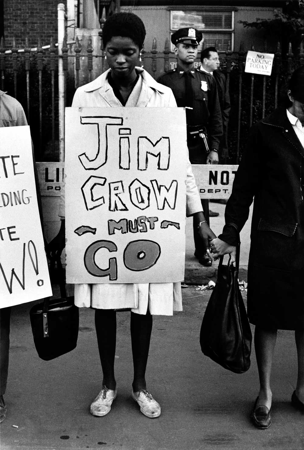 A woman stands in a line of protesters holding hands, with a sign around her that says “Jim Crow must go”