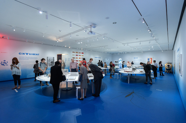 Installation Shot of Germ City: Microbes and the Metropolis, with a crowd looking at the exhibition.