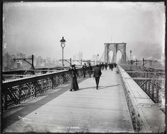 A black and white photograph of people walking along the Brooklyn Bridge in 1903