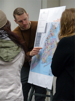 Participants discuss a map using different color pins and beads to show their borough of residence, length of commute, and workplace location to analyze commuting patterns.