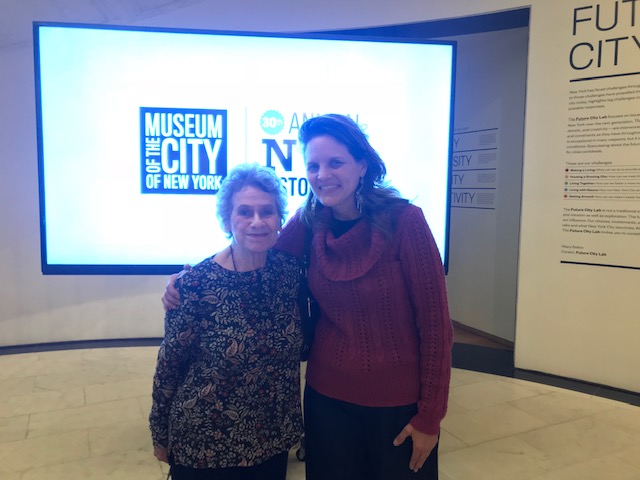 Two women stand together in front of a screen with the logos for the Museum and History Day.