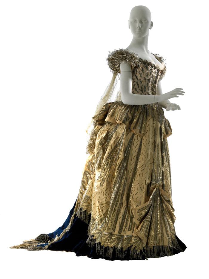 A gold floor-length dress with metallic details, a black underskirt, and blue train