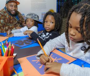 A man and three young children make art at a table.