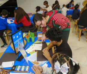 A woman helps a young child with an art project at a table. 