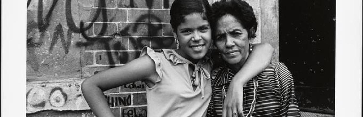 Two women pose in front of a graffitied building in the South Bronx of New York City