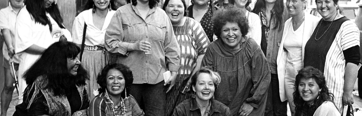 Photograph of artists from the exhibition, Women of Sweetgrass, Cedar and Sage, friends and community members outside the American Indian Community House Gallery taken in 1985. 