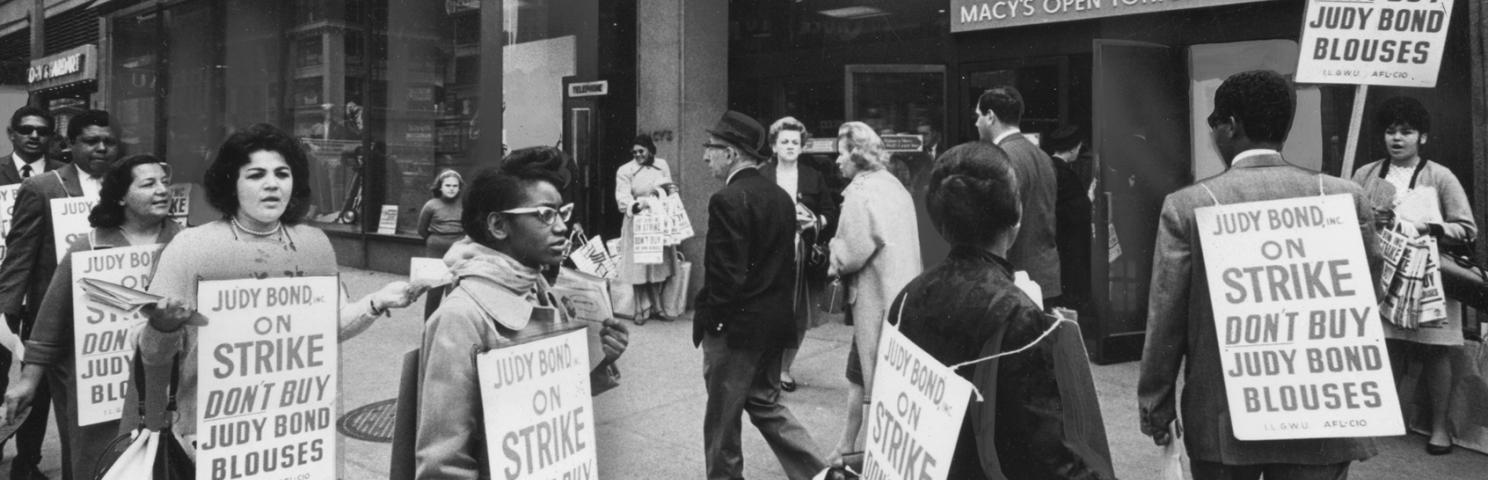 A group of on-strike workers march outside Macy’s while wearing signs encouraging people to not buy Judy Bond blouses 