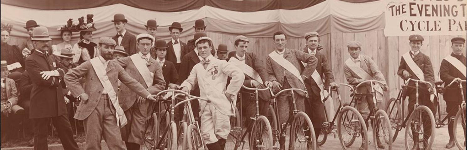 Men line up with their bicycles as spectators look on from raised seating before The Evening Telegram Bicycle Parade