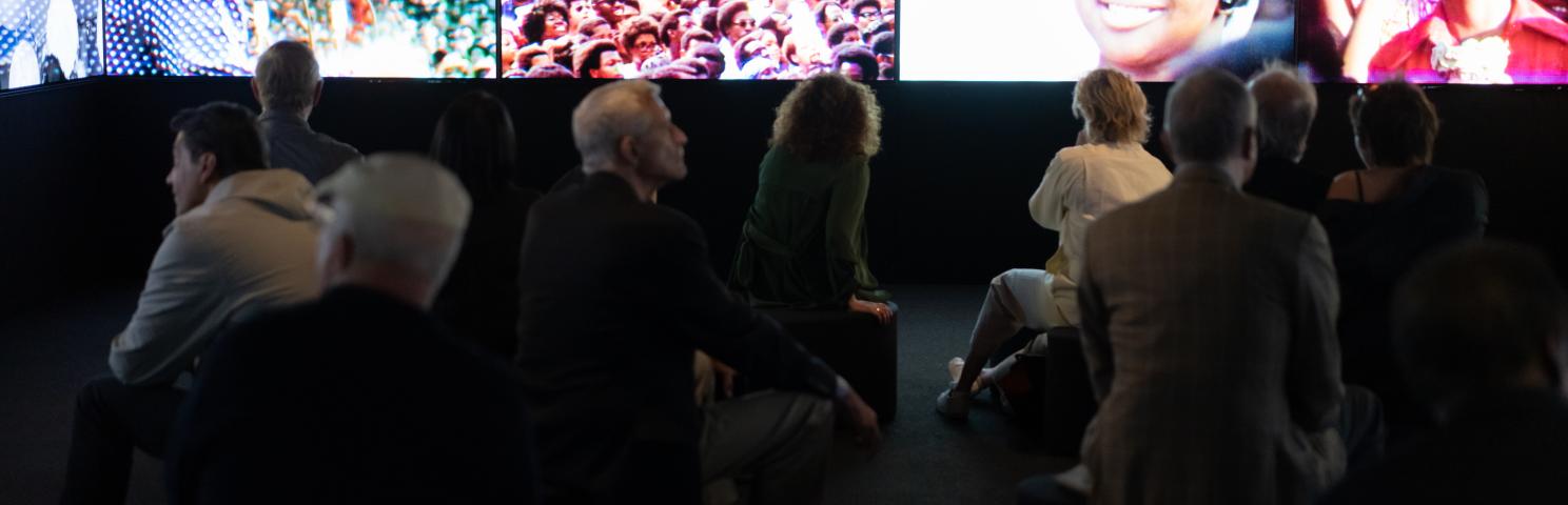 Several people watching a multi-screen film about New York