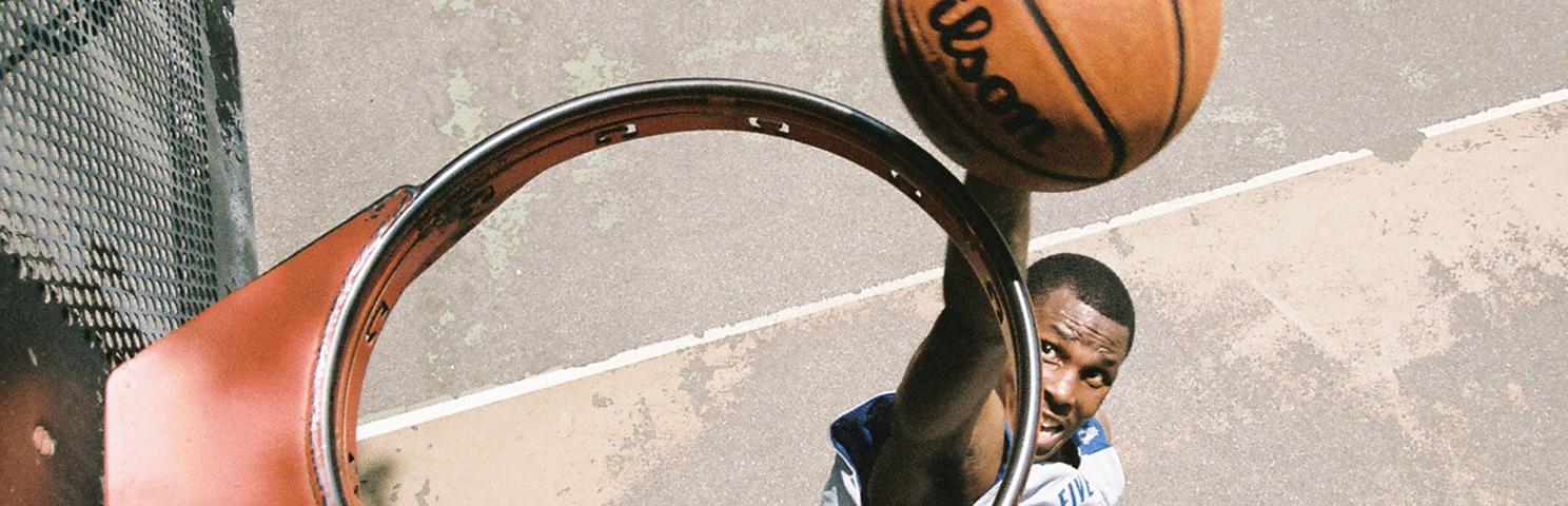 View from above a basketball hoop without a net, where a player is seen about to dunk a basketball through the hoop