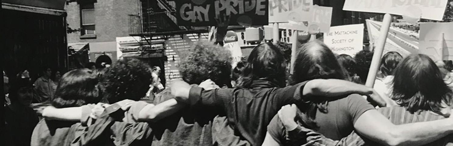 Photograph by Fred W. McDarrah of a group of people with their arms around each other and holding signs related to Pride