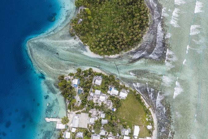 Ejit Island as seen from above. The ocean cuts through two lush green landmasses—with structures visible on the one towards the bottom of the image, and enters into a deep blue patch of ocean. 