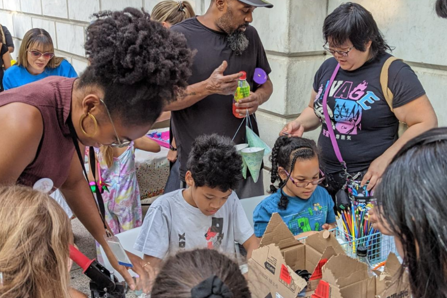 A group of young people stand around a table making crafts with instructors.