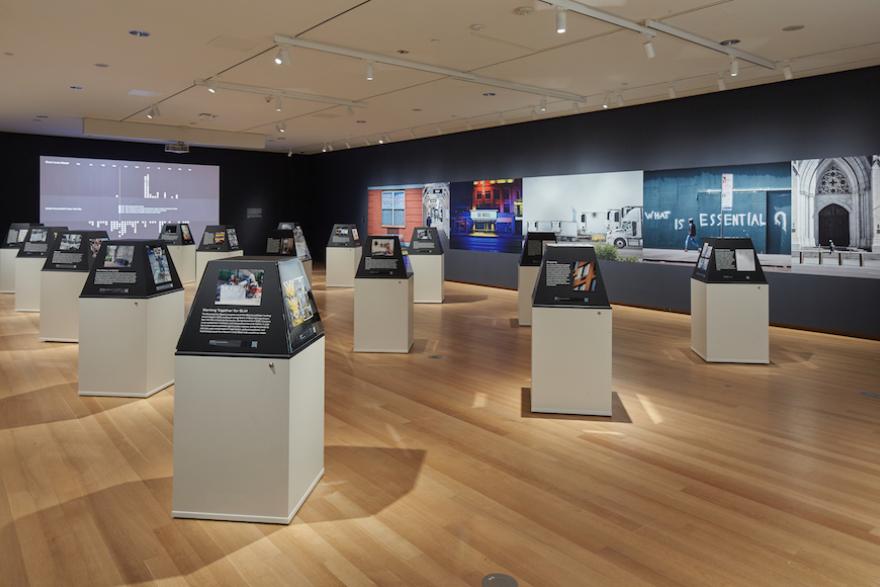 Installation Shot of New York Responds: The First Six Months. View of the main exhibition space with 15 plinths holding objects and images, and some images visible on the walls.