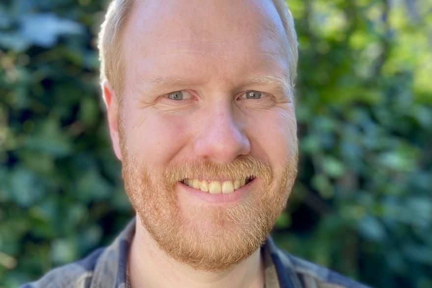 A man in a plaid shirt smile at the camera. 