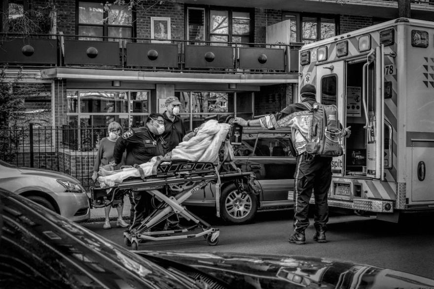 A person on a stretcher is being wheeled into an ambulance assisted by three medical workers. A fourth person stands nearby.