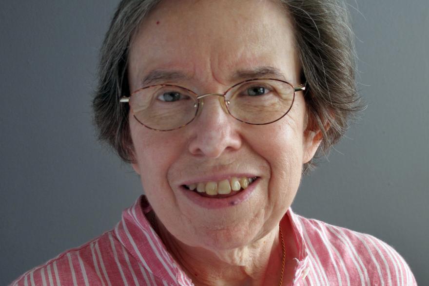 A woman in glasses and a pink shirt smiles at the camera. 