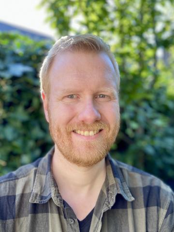 A man in a plaid shirt smile at the camera. 