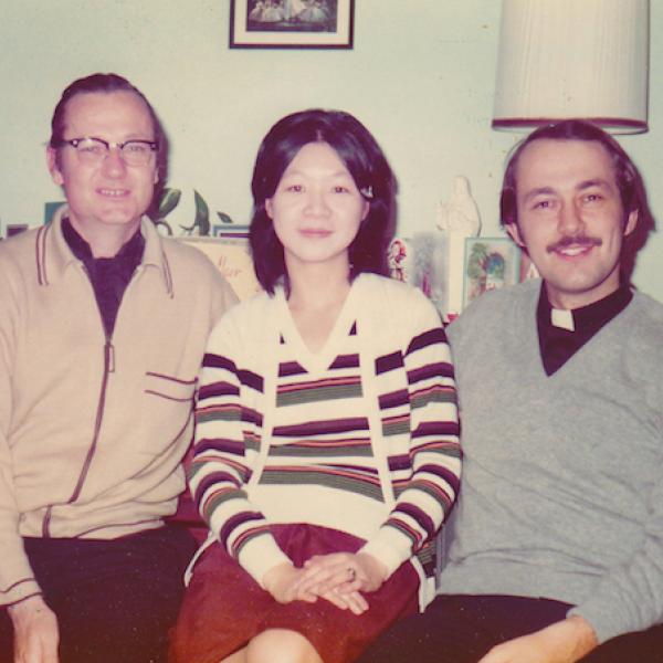 Color photograph of Fathers Denis Hanly (right) Joanna Chan, and Richard Grillo (left), sitting in a living room.