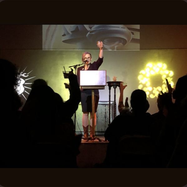 Image of woman dressed in black holding a glass cup for a toast with audience clapping in front of her and a graphic background behind her