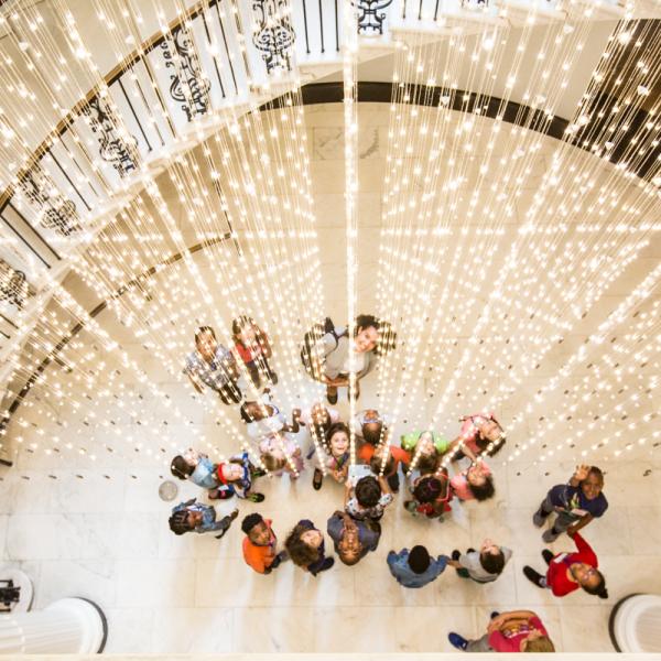 A group of students stand under the Museum's light installation, "Starlight."