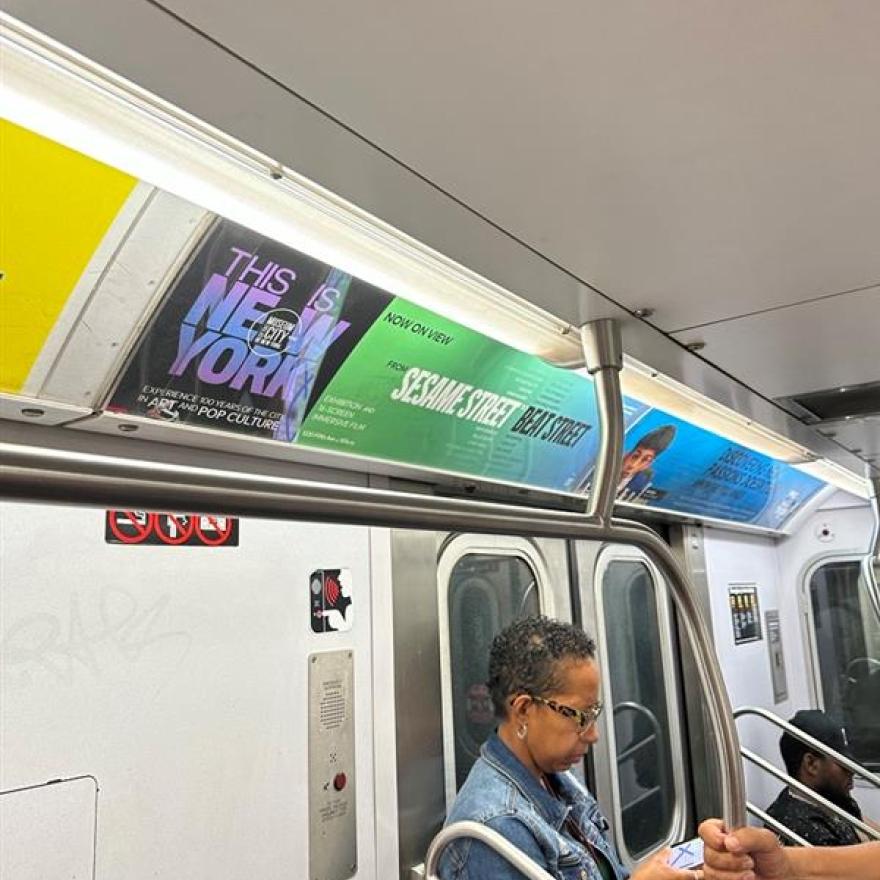 Subway ad for the exhibition "This Is New York" above the door in a subway car.