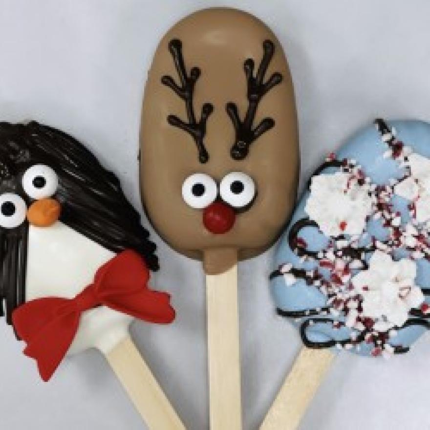 Three winter holiday themed cakesicles. From left to right: a penguin cakesicle, a reindeer cakesicle, and a winter-inspired cakesicle.