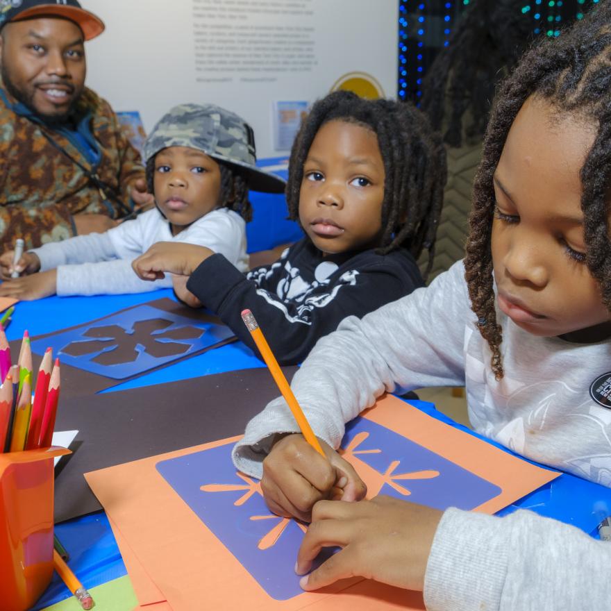 A man and three young children make art at a table.