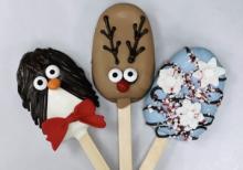 Three winter holiday themed cakesicles. From left to right: a penguin cakesicle, a reindeer cakesicle, and a winter-inspired cakesicle.