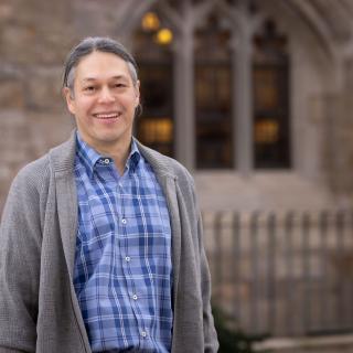 A portrait of Dr. New Blackhawk weather a gray cardigan and a blue patterned shirt.