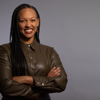 Woman smiling with her arms crossed in front of a grey backdrop 