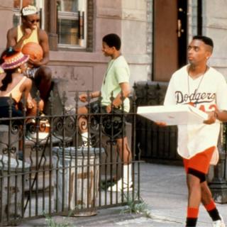 Spike Lee as Mookie walks down a Bedford-Stuyvesant street carrying a pizza