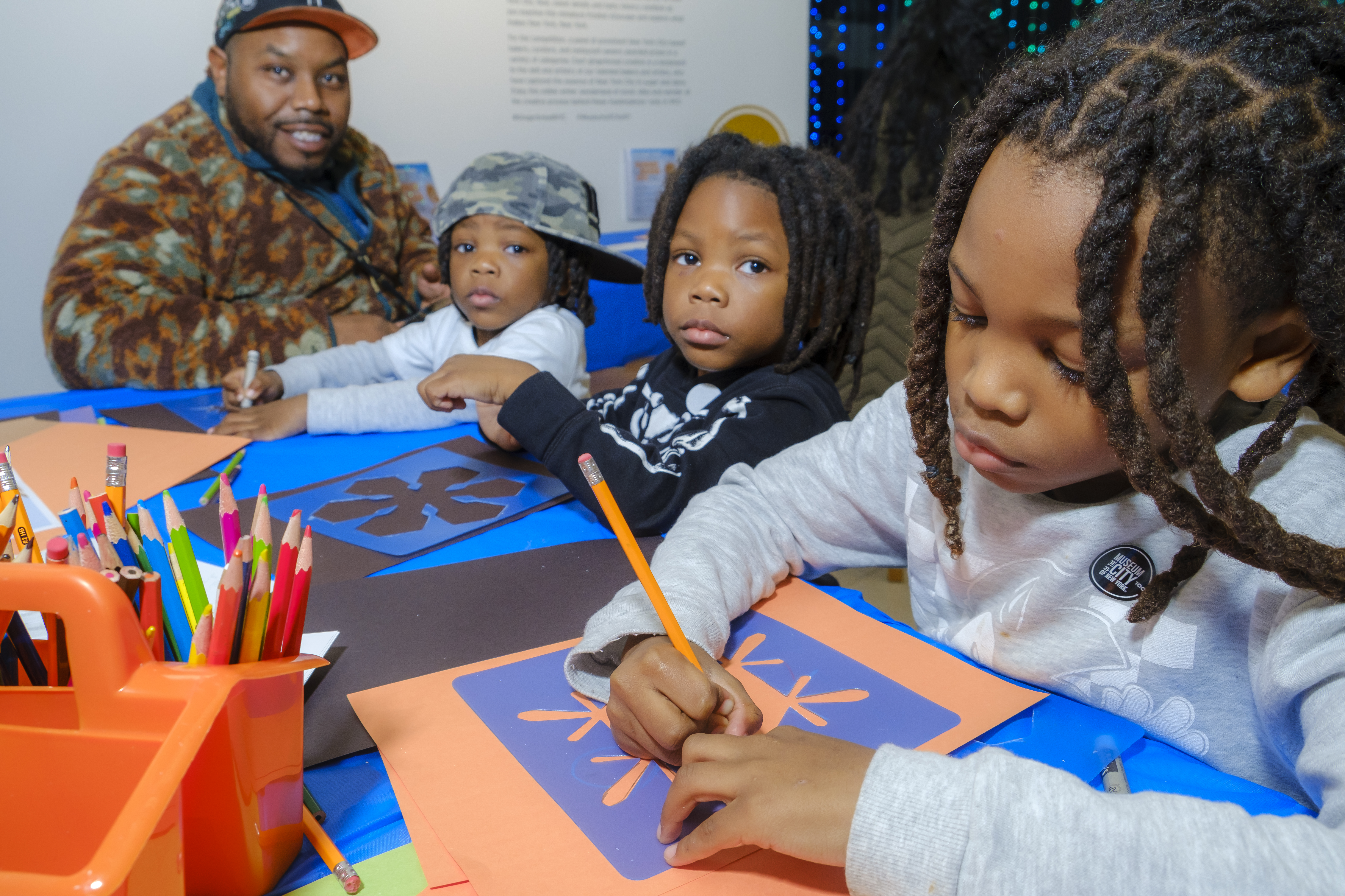 A man and three young children make art at a table.