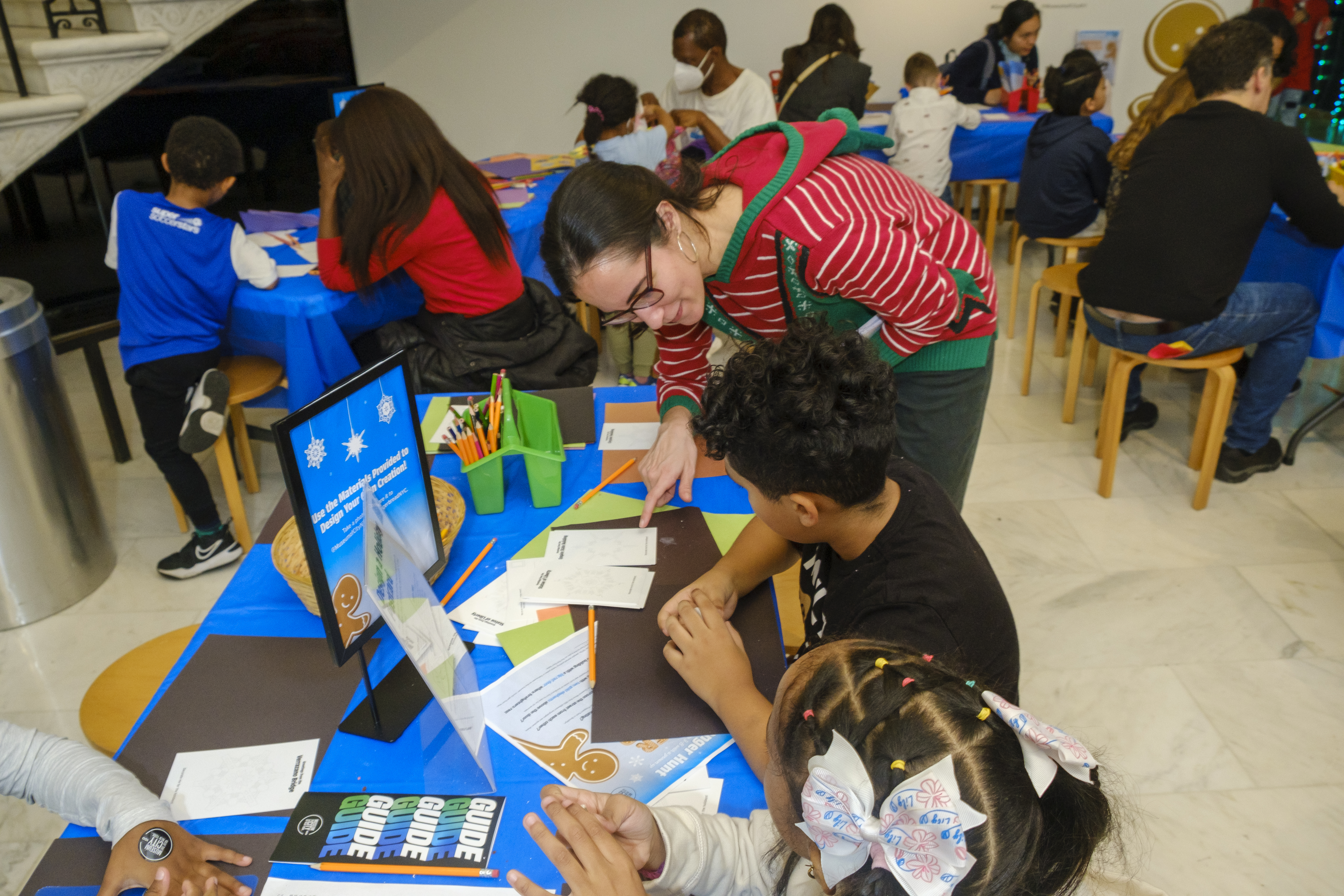 A woman helps a young child with an art project at a table. 